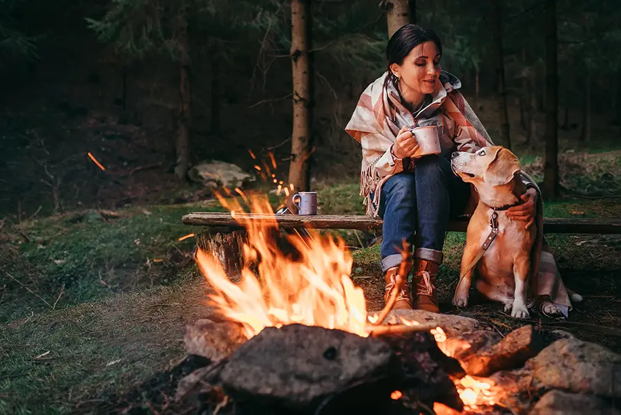 Woman sitting with her dog beside a campfire